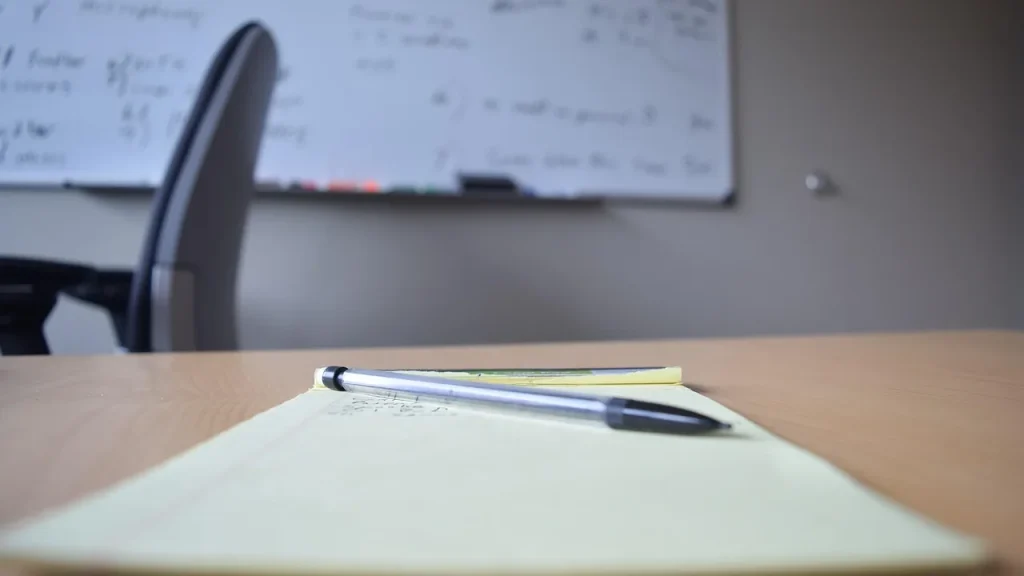 A table covered with forms and documents, a pen and a laptop visible.