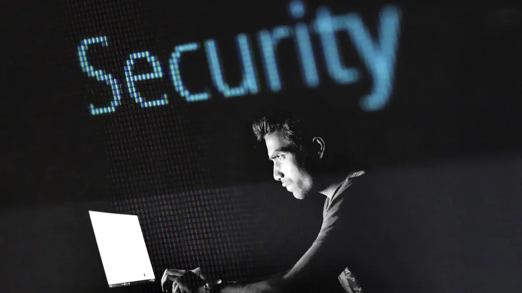 A person typing on a laptop with a privacy screen, blurred data in the background