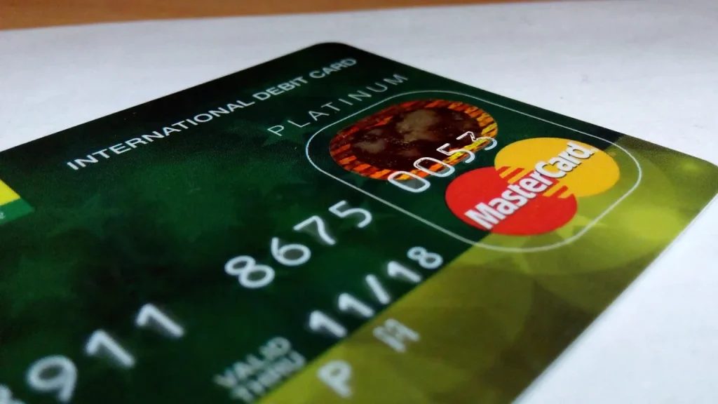 Hand holding a credit card near a laptop showing numbers and a globe