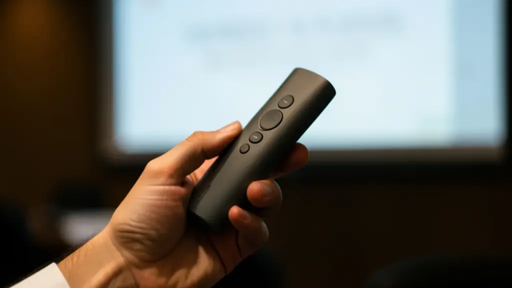 A hand holding a slide clicker in a dim conference room