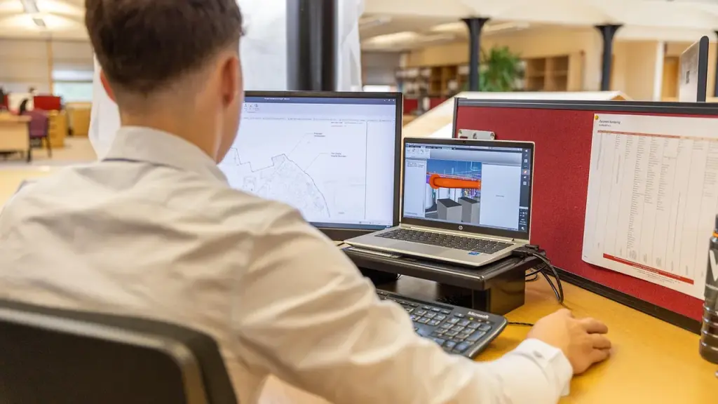 A developer uses a laptop with multiple monitors showing graphs and code.
