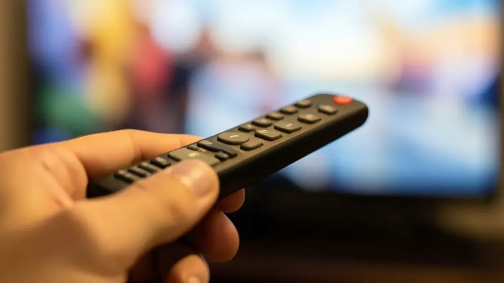 A hand holding a TV remote toward a blurred screen