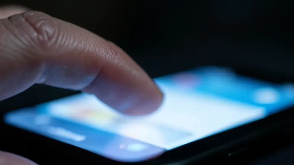 A thumb hovering over a blurred smartphone screen in a dim room