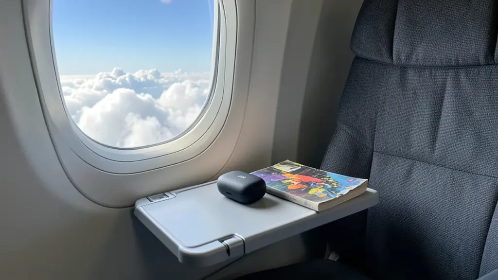 An earbud case on an airplane tray table by the window