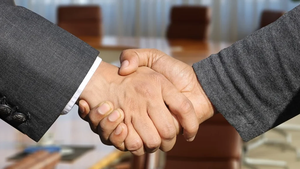 Two professionals shake hands in a startup-style tech office